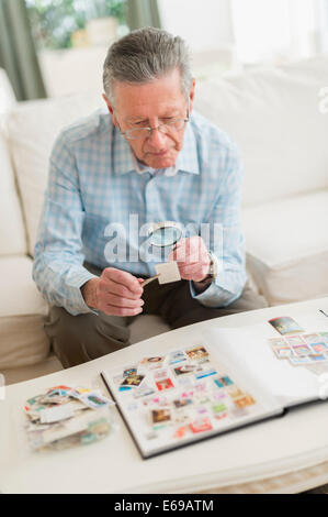 Senior uomo caucasico esaminando raccolta di francobolli Foto Stock