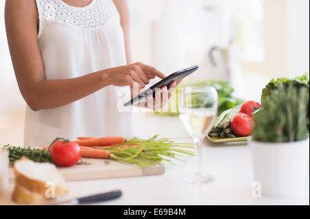 Donna ispanica cucinare con tavoletta digitale in cucina Foto Stock