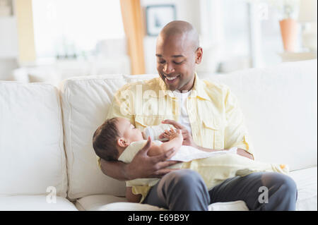 Padre sorridente alimentazione bambino sul divano Foto Stock