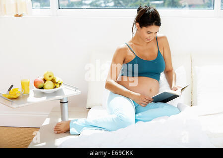 Incinta donna ispanica lettura a letto Foto Stock