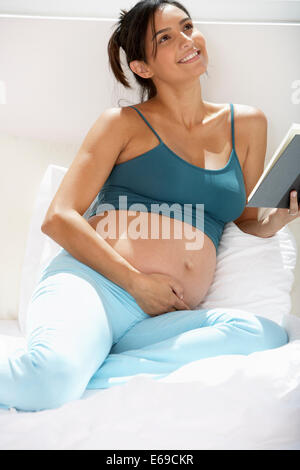 Incinta donna ispanica lettura a letto Foto Stock