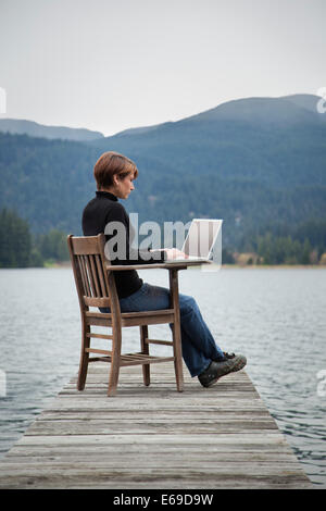 La donna caucasica utilizzando laptop sul dock in legno sul lago Foto Stock