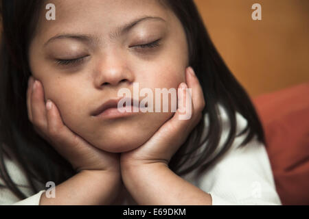 Razza mista la sindrome di Down girl appoggiato con il mento in mani Foto Stock