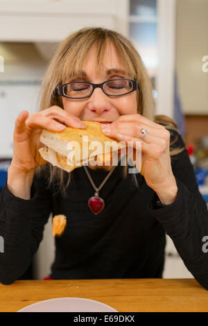 La donna caucasica mangiare panino in cucina Foto Stock