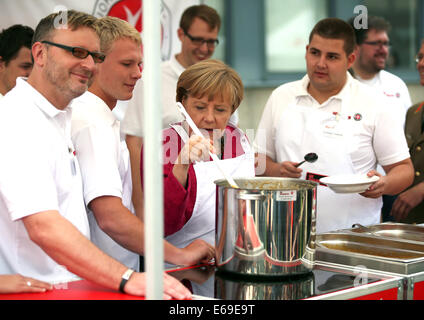 Bonn, Germania. 19 Ago, 2014. Il cancelliere tedesco Angela Merkel (C) suscita uno stufato in una cucina di campo dell'Ordine di San Giovanni di Bonn, Germania, 19 agosto 2014. Il cancelliere tedesco ha visitato l'Ufficio federale della protezione civile e di assistenza di emergenza per conoscere il lavoro di ufficio e dell'Agenzia federale per il rilievo tecnico (THW). Foto: OLIVER BERG/DPA/Alamy Live News Foto Stock