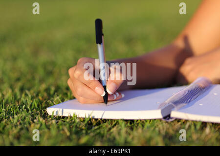 In prossimità di una donna la scrittura a mano su un notebook outdoor sdraiati sull'erba in un parco Foto Stock