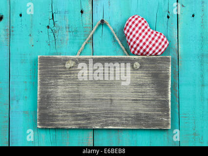 Vuoto segno invecchiato con rosso a scacchi cuore appeso su antichi rustici teal blu porta in legno Foto Stock