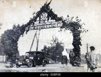 Agosto 18, 2014 - Il veicolo passa sotto l'Arc de Triomphe con l'Ucraino stemma decorato con fiori e uno striscione con la scritta ''Gloria in Ucraina. Bandera Gloria!" in ucraino e tedesco, Ucraina Occidentale, 1941. La riproduzione di antichi foto © Igor Golovniov/ZUMA filo/Alamy Live News Foto Stock