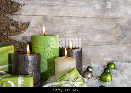 Quattro burning avvento candele in verde e marrone in legno su sfondo grigio. Foto Stock