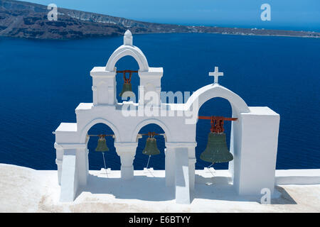 Vista sul mare calmo superficie attraverso la tradizionale greco bianco arco della Chiesa con la croce e le campane nel villaggio di Oia delle Cicladi Isola Sant Foto Stock