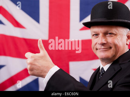 Imprenditore britannico, indossando un cappello bowler e dando il pollice in alto segnale, mentre nella parte anteriore della Union Jack bandiera nazionale. Foto Stock