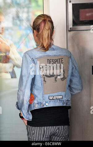 Giovane donna che indossa nonostante tutto giacca in denim guardando attraverso ascensore di vetro con l'uomo sul lato opposto a Londra, Regno Unito nel mese di agosto Foto Stock