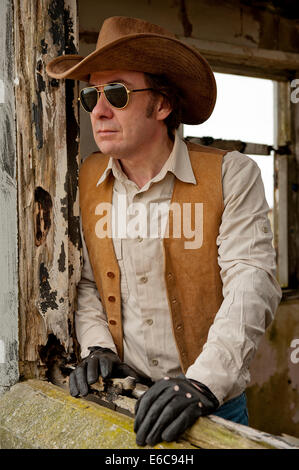 Il giorno moderno cowboy, guardando fuori della finestra di un edificio abbandonato. Foto Stock