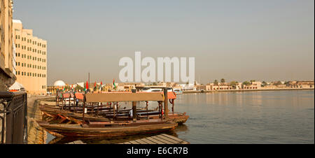 Barche in legno, abras tradizionali utilizzate come piccoli trasporti pubblici traghetti, sul Dubai Creek con edifici in background nella città di Dubai Foto Stock