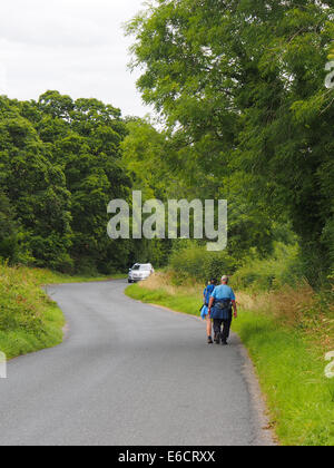 Gli escursionisti a piedi a lato di un vicolo del paese senza marciapiede come una macchina si avvicina da dietro un angolo Foto Stock