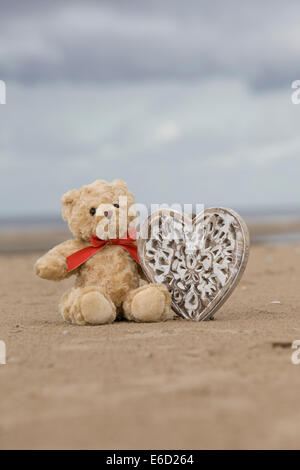 Orsacchiotto di peluche sulla spiaggia con un cuore di legno Foto Stock