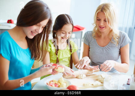 Due ragazze preparare il cibo con la loro madre Foto Stock