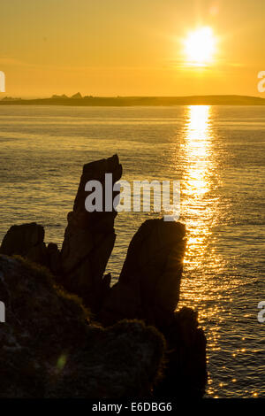 Le formazioni rocciose intorno alla costa di Sant'Agnese si stagliano contro il sole mentre tramonta sull'isola di Annet. Foto Stock