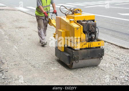 Lavoratore di vibrazione di pilotaggio compattatore a rulli sul marciapiede di riparazione Foto Stock