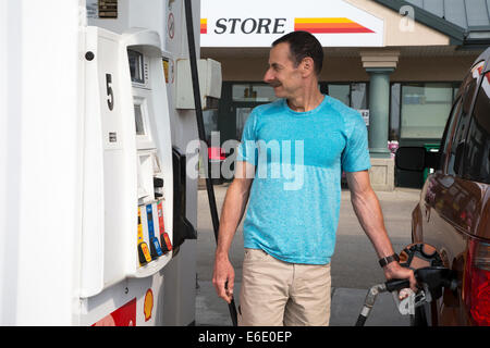 Uomo che pompa gas nel suo veicolo mentre guarda il prezzo mostra in una stazione di servizio in Alberta, Canada Foto Stock