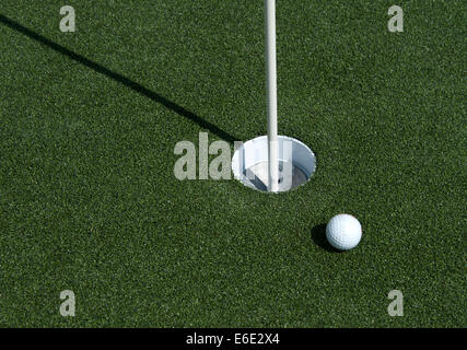 Una pallina da golf si siede vicino al foro sul putting green Foto Stock