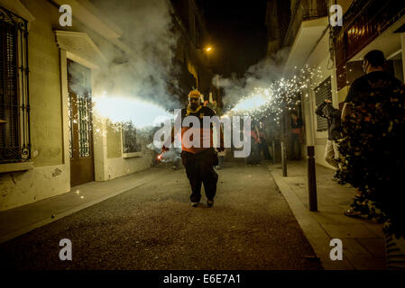 Barcellona, Spagna. 21 Ago, 2014. Un membro di 'la Vella de Gracia' scorre di fronte i petardi del 'Dragon di Gracia' durante il 'Correfocs' a 'Festa Major de Gracia'. - La Festa Major de Gracia, uno della Barcellona più vivaci festival, termina con correfocs (fire-corre), una delle caratteristiche più impressionanti in catalano festival. Tradizionalmente le strade sono prese in consegna dai bambini vestiti in costumi del diavolo. Credito: Matthias Oesterle/ZUMA filo/ZUMAPRESS.com/Alamy Live News Foto Stock