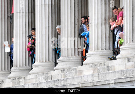 Londra, Inghilterra, Regno Unito. Trafalgar Square. persone tra le colonne della Galleria Nazionale, guardare gli spettacoli degli artisti di strada al di sotto di Foto Stock
