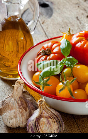 Appena raccolto i pomodori in una ciotola di smalto di carne, aglio, basilico e una bottiglia di olio di oliva Foto Stock