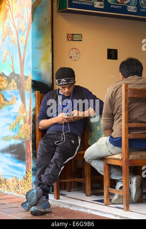 BANOS, ECUADOR - 25 febbraio 2014: Unidentified giovane con auricolari e un dispositivo elettrico seduti ad un ristorante Foto Stock