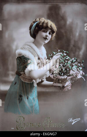 Cartolina d'epoca con una donna in abito elegante che tiene fiori in un giardino dell'inizio del XX secolo Foto Stock