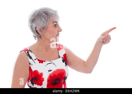 Attraente donna anziana isolato su bianco e indossando un vestito estivo puntando con il dito. Foto Stock