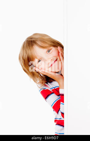 Ragazzo con capelli biondi che spuntavano da dietro un pannello bianco sorridente Foto Stock