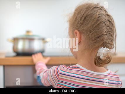 Bambino tocca padella calda sul fornello. Situazione di pericolo a casa. Foto Stock