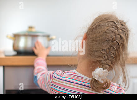 Bambino tocca padella calda sul fornello. Situazione di pericolo a casa. Foto Stock