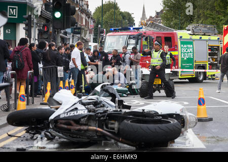 Londra, Regno Unito. 24 Agosto, 2014. Paramedici e vigili del fuoco di occuparsi di un ferito biker che sembrava avere eseguito nel retro di un auto in corrispondenza dell'intersezione di Chamberlayne Road e Harvist strada in Kensal Green. Un certo numero di motociclisti era stato ruggente su e giù per la strada come primo giorno del carnevale di Notting Hill è venuto a una stretta. Credito: Paolo Davey/Alamy Live News Foto Stock