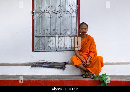 Un giovane debuttante monaco buddista seduti al sole del pomeriggio presso il monastero. Luang Prabang, Laos. Modello rilasciato. Foto Stock