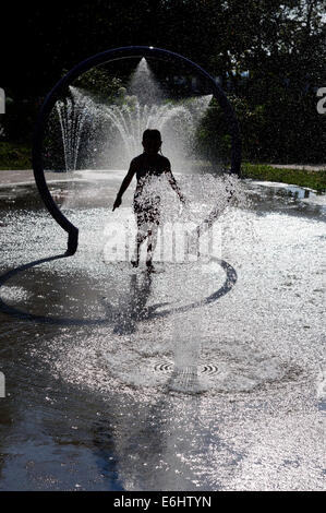 Una giovane ragazza che gioca in acqua delle fontane in una calda giornata estiva Foto Stock