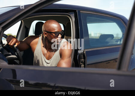 Immagine del bel giovane uomo seduto in macchina guardando lontano. Afro American modello maschile seduto in auto. Uomo muscolare sul viaggio. Foto Stock