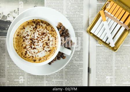 Tazza di caffè torrefatto in grani e sigarette disposte su un giornale Foto Stock