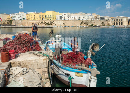 I pescatori riassettavano le reti da pesca e le imbarcazioni di pulizia presso il molo nel centro storico di Gallipoli, Puglia, Italia meridionale. Foto Stock