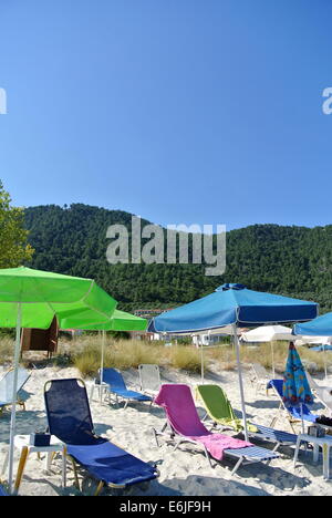 Sedie a sdraio con ombrelloni, cielo blu, montagna, in Thassos, Grecia Foto Stock