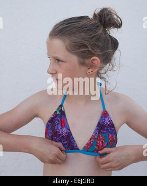 Giovane ragazza caucasica indossando un bikini guardando alla sua destra regolando il suo bikini top Foto Stock