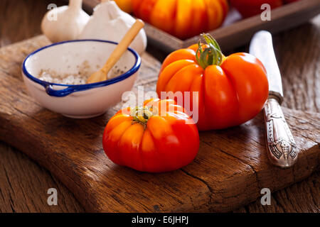 Carni bovine mature pomodori dal proprio giardino con la lama di un coltello e sale su un rustico tagliere Foto Stock