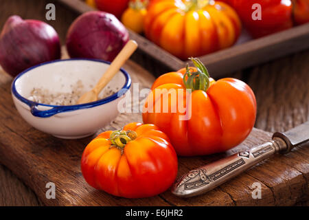 Carni bovine mature pomodori dal proprio giardino con la lama di un coltello, cipolle e sale su un vecchio rustico tagliere in stile country Foto Stock