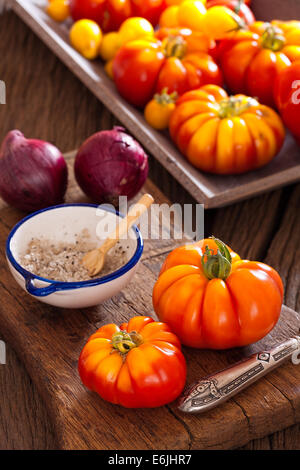 Carni bovine mature pomodori dal proprio giardino con la lama di un coltello, cipolle e sale su un vecchio rustico tagliere in stile country Foto Stock