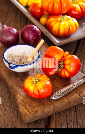 Carni bovine fresche pomodori dal proprio giardino con la lama di un coltello, cipolle e sale su un vecchio rustico tagliere in stile country Foto Stock