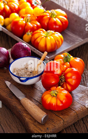 Carni bovine mature pomodori dal proprio giardino con la lama di un coltello, cipolle e sale cantina in un vecchio rustico tagliere in stile country Foto Stock