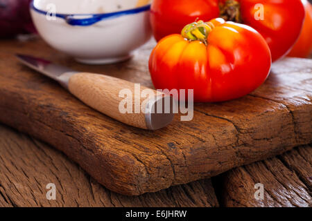 Close up di un maturo bistecca di manzo pomodoro dal proprio giardino e un coltello da cucina su un rustico tagliere in stile country Foto Stock