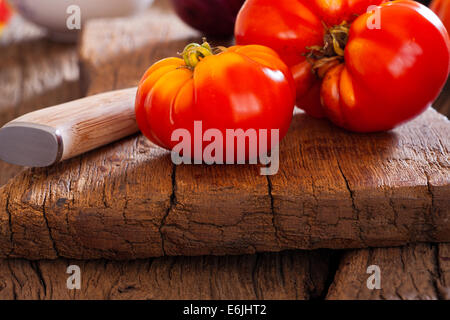 Close up di un maturo bistecca di manzo pomodoro dal proprio giardino e un coltello da cucina su un rustico tagliere in stile country Foto Stock