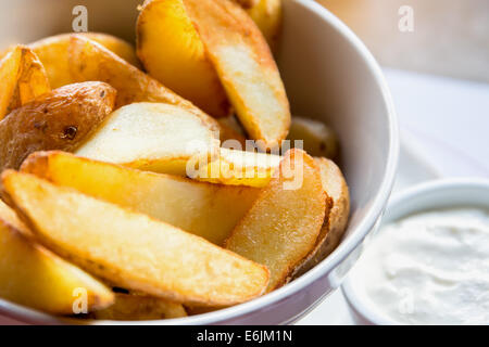 Patate fritte cunei in una ciotola con il bianco salsa di aglio Foto Stock